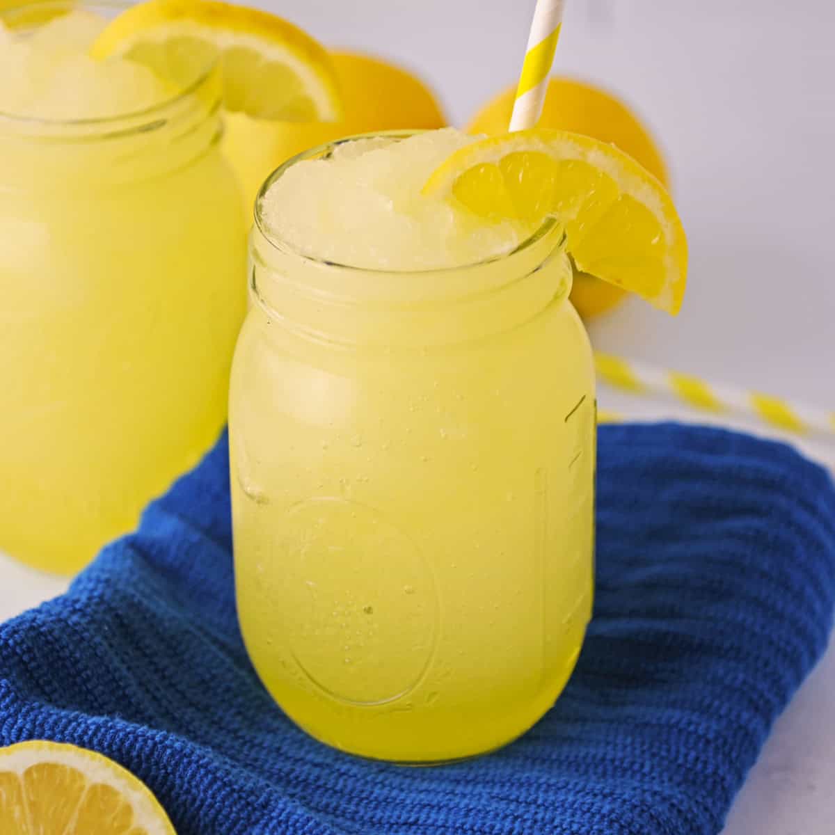 Frozen lemonade slushies garnished with slice of lemon and served in mason jars with yellow striped straws.