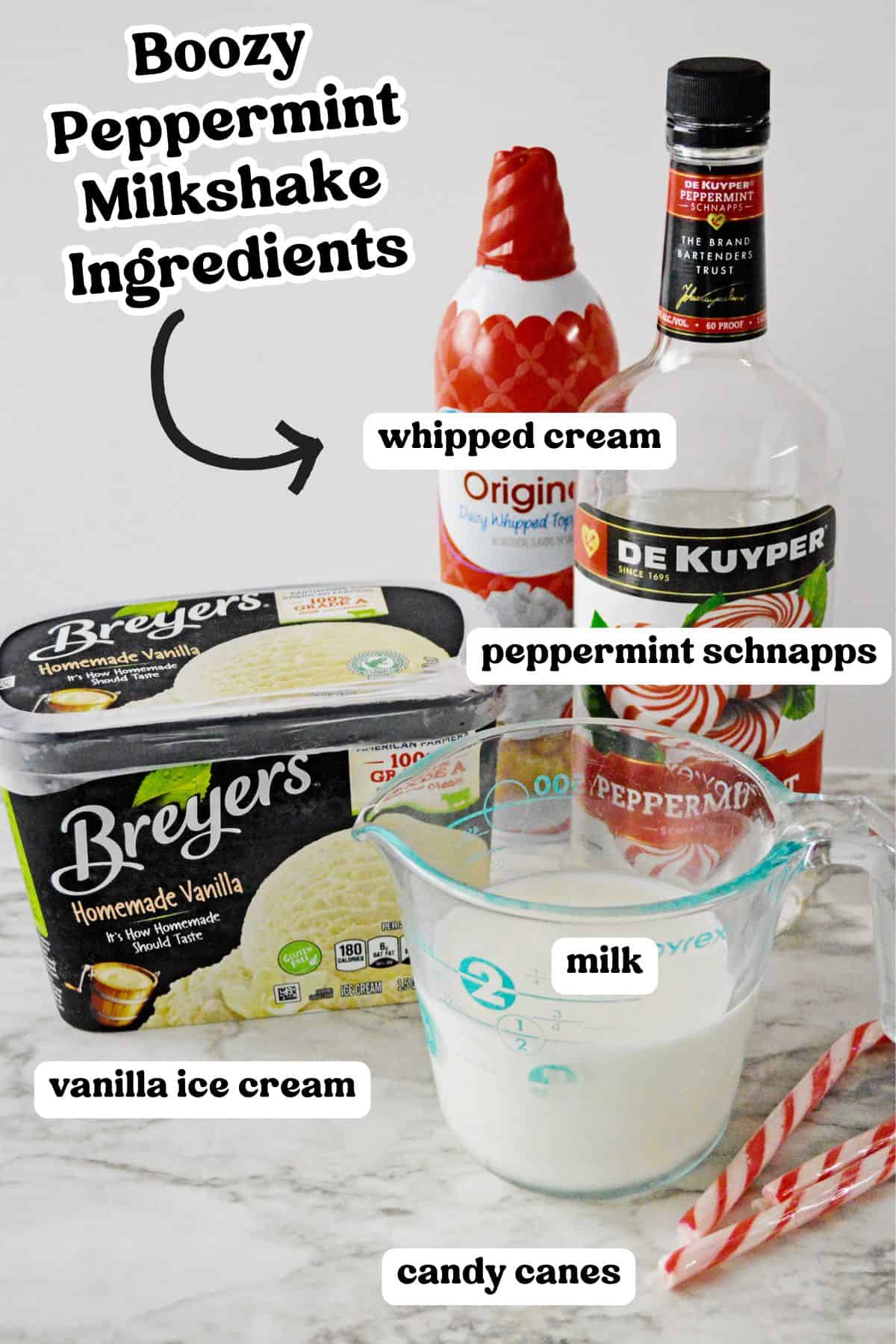 Ingredients for a boozy peppermint milkshake arranged on a counter: Breyers vanilla ice cream, a bottle of peppermint schnapps, whipped cream, a measuring cup of milk, and candy canes.