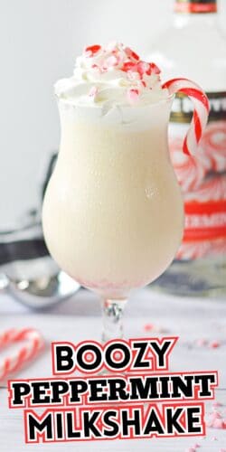 Boozy peppermint milkshake in a curved glass, topped with whipped cream, crushed candy canes, and a candy cane garnish.