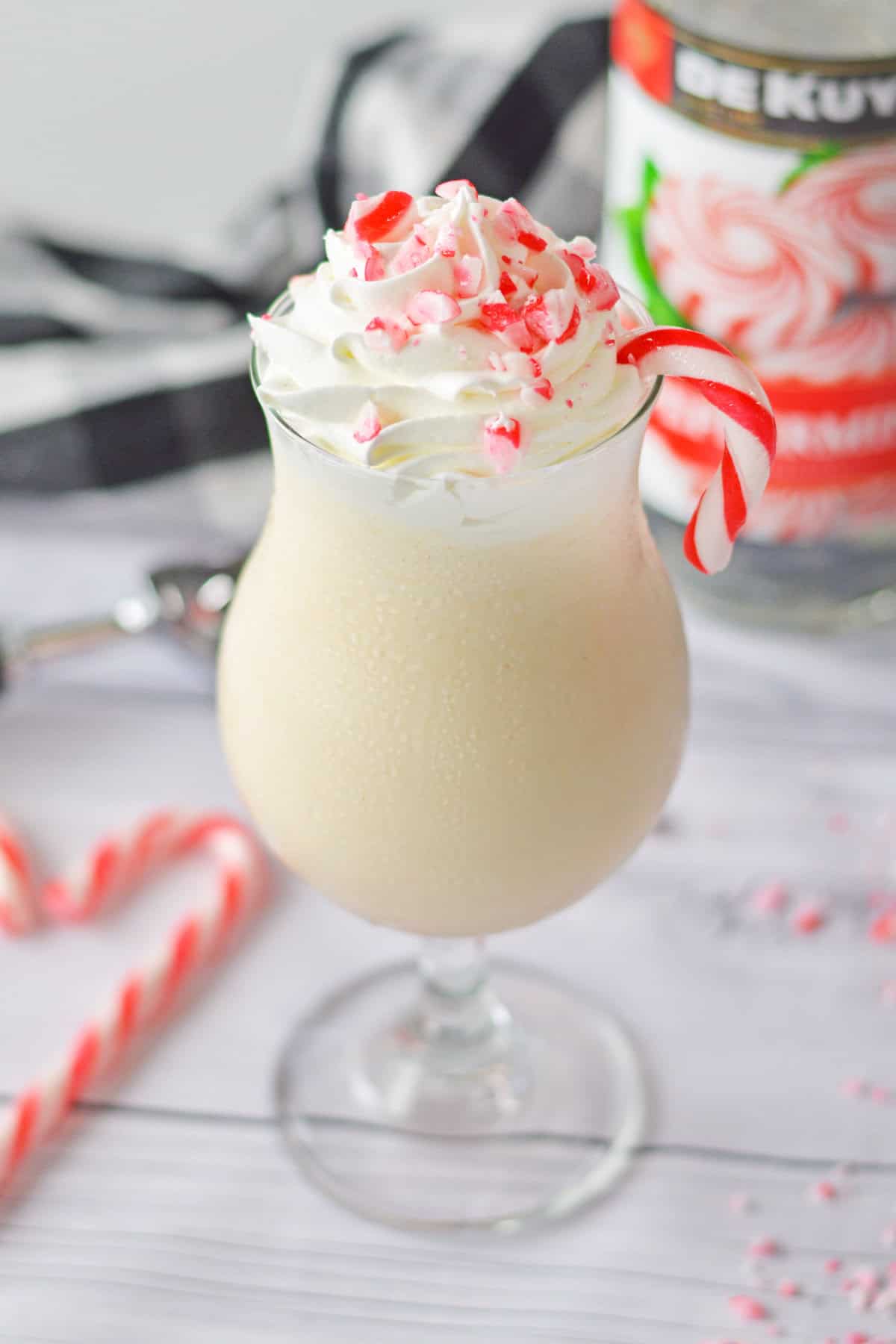 A creamy boozy peppermint milkshake in a glass, topped with whipped cream, crushed peppermint candies, and a candy cane garnish and a festive background.