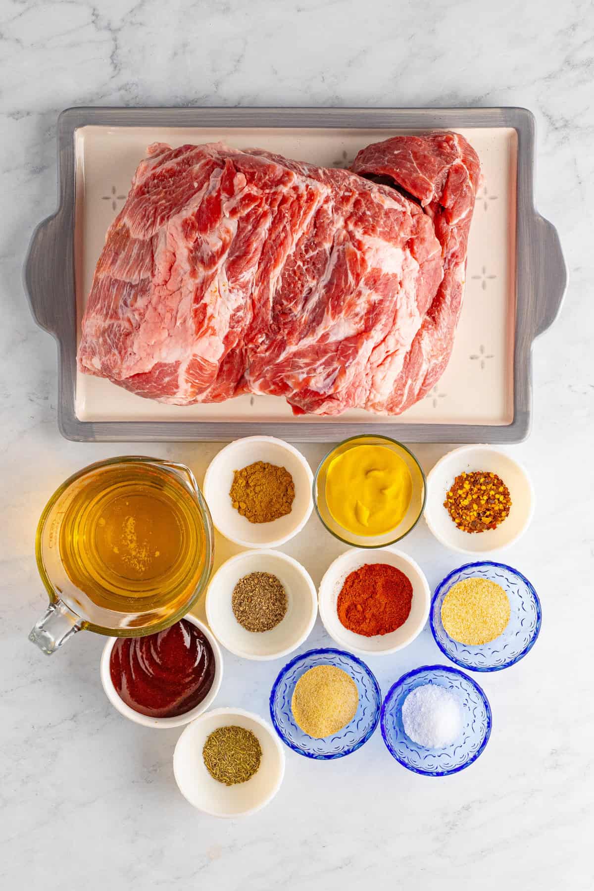 A raw pork shoulder with seasonings and sauces arranged around it.