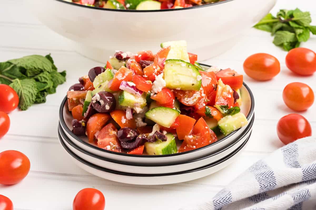 A serving of Greek salad in a small, stacked bowl, filled with chopped cucumbers, cherry tomatoes, red bell peppers, kalamata olives, red onion, crumbled feta, and mint.
