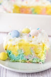A slice of pastel Easter poke cake topped with whipped cream, coconut, and mini chocolate eggs.