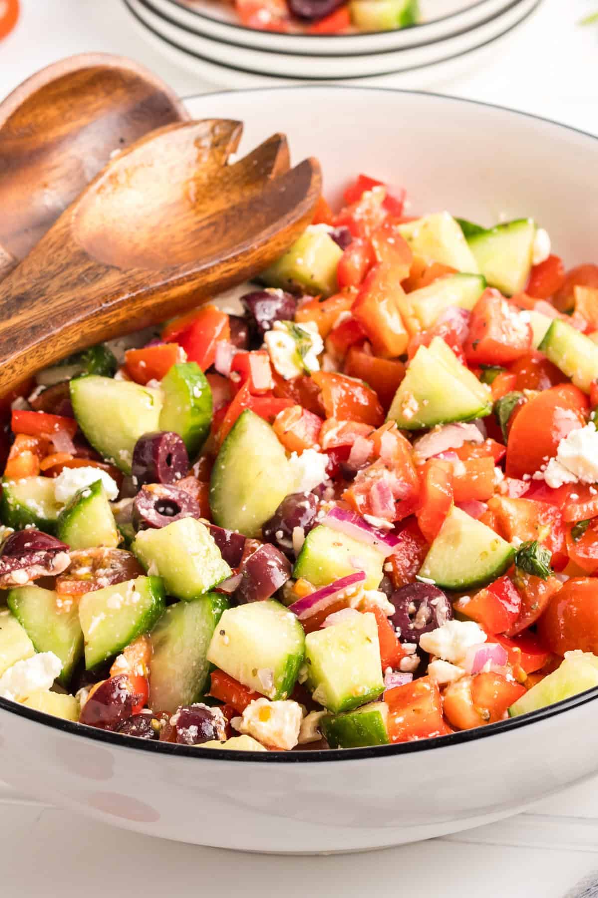 A large bowl filled with Greek salad, showcasing chopped cucumbers, cherry tomatoes, red bell peppers, kalamata olives, red onion, crumbled feta, and mint.