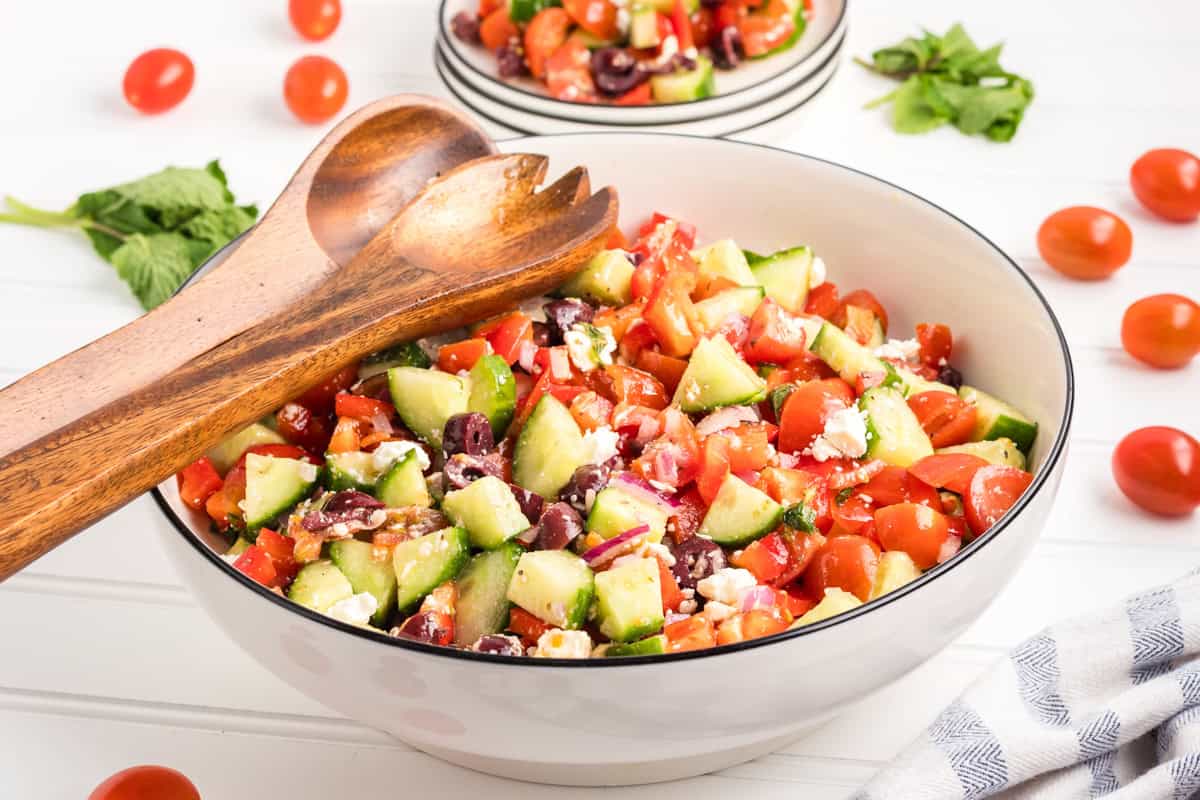 A large bowl of Greek chopped salad with wooden salad servers resting on top.
