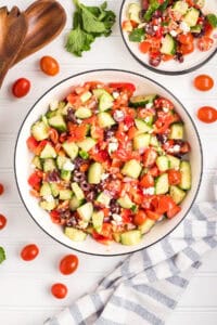 A top-down view of a large bowl of chopped Greek salad with a smaller serving bowl nearby.