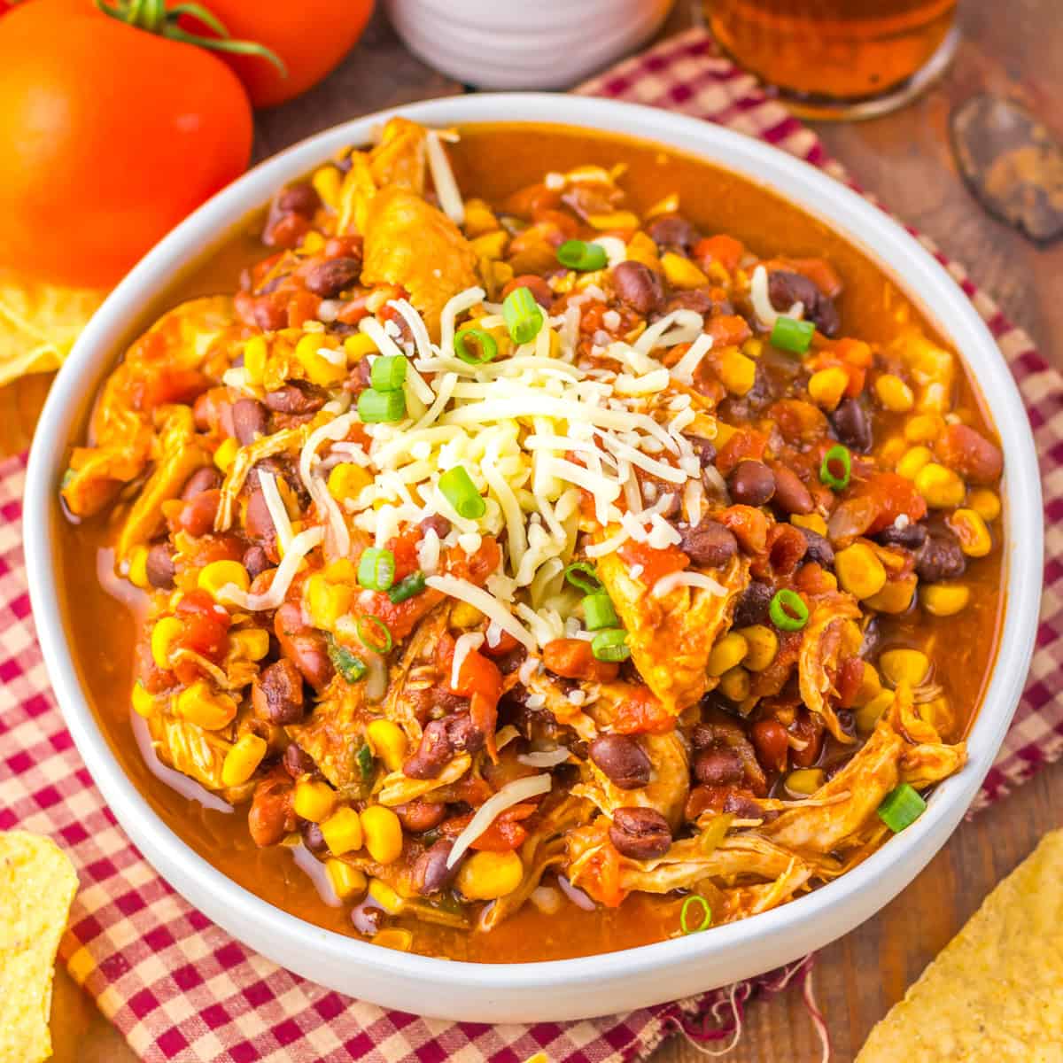 A bowl of chicken taco soup recipe topped with shredded cheese and green onions, surrounded by tortilla chips.