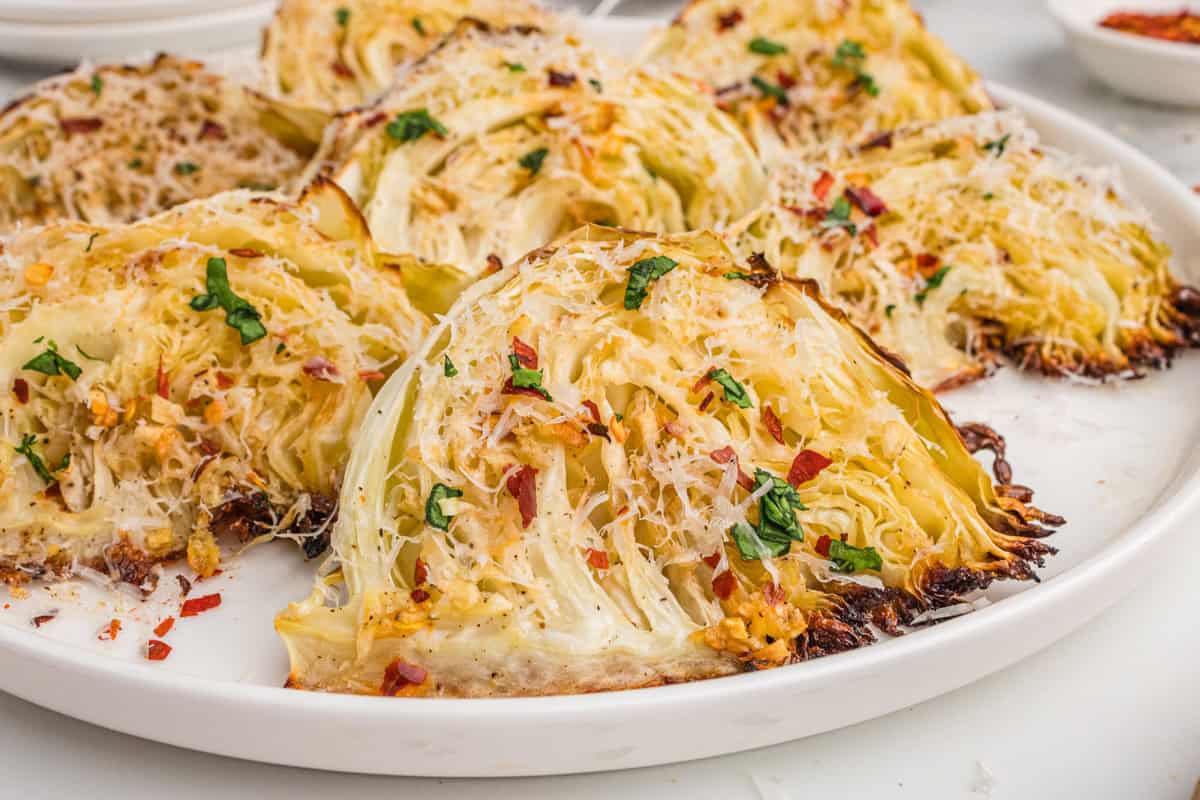 Close-up of roasted garlic parmesan cabbage wedges on a white plate, topped with shredded parmesan, parsley, and red pepper flakes.