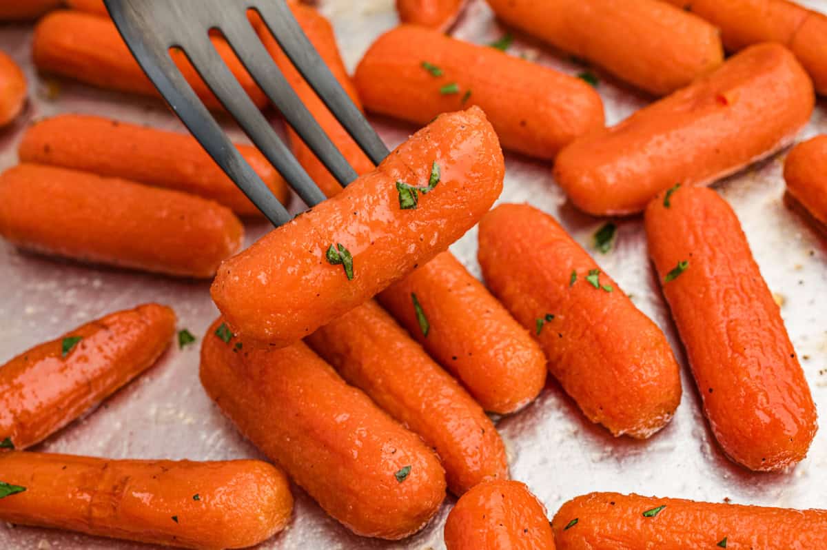 A fork lifting a glazed carrot from a tray of roasted brown sugar baby carrots.
