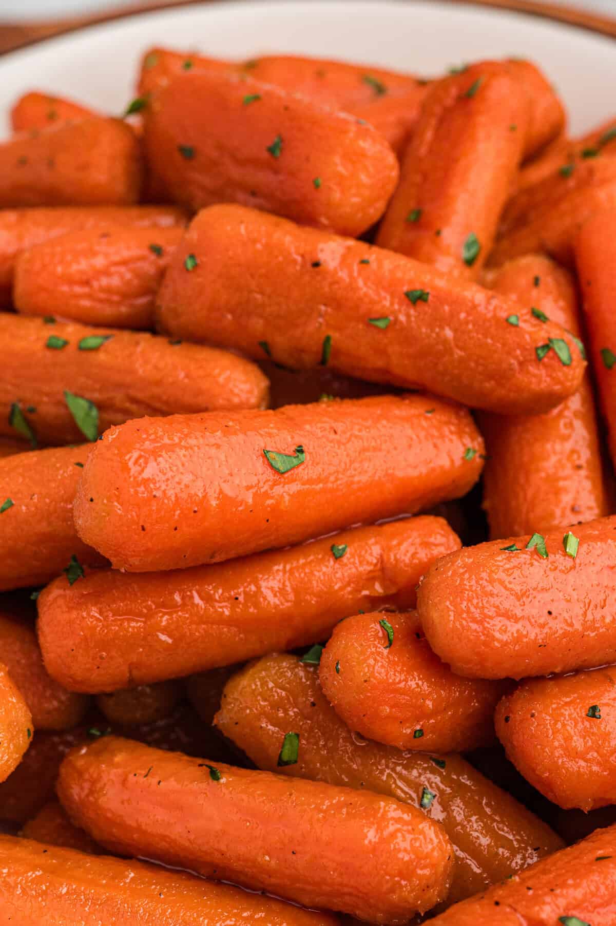A close-up of brown sugar honey glazed carrots garnished with chopped herbs.