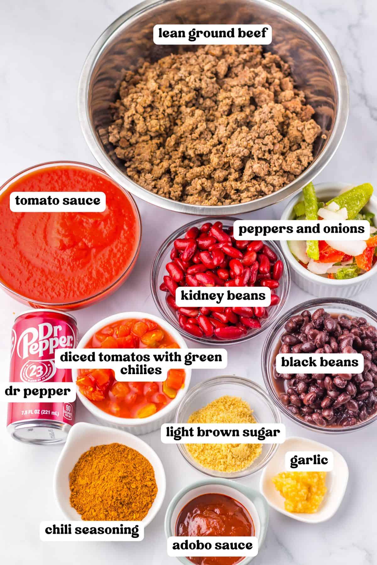 Ingredients for Dr Pepper chili, including ground beef, tomato sauce, kidney beans, black beans, peppers and onions, diced tomatoes with green chilies, light brown sugar, garlic, chili seasoning, adobo sauce and a can of Dr Pepper.