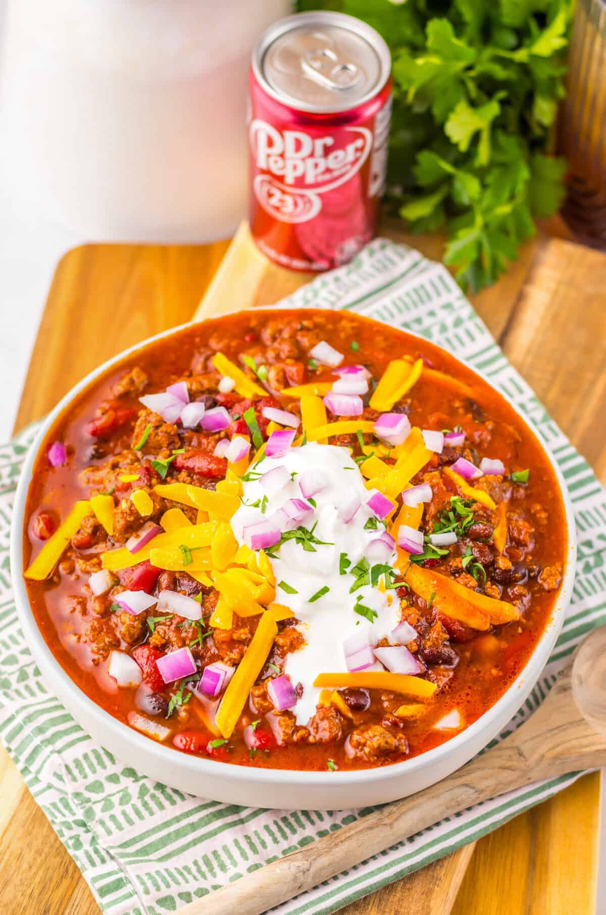 Bowl of crockpot Dr pepper chili with toppings next to a can of Dr Pepper.