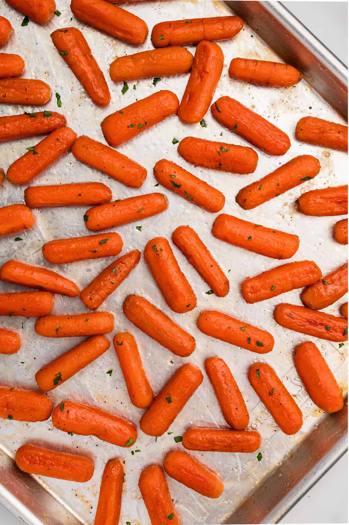 A sheet pan filled with a single layer or roasted baby carrots coated in a brown sugar honey glaze.