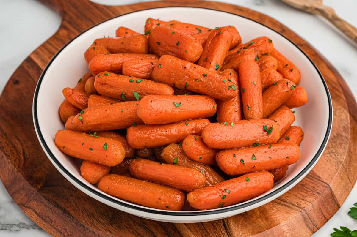 A bowl of glazed brown sugar baby carrots on a wooden serving board.