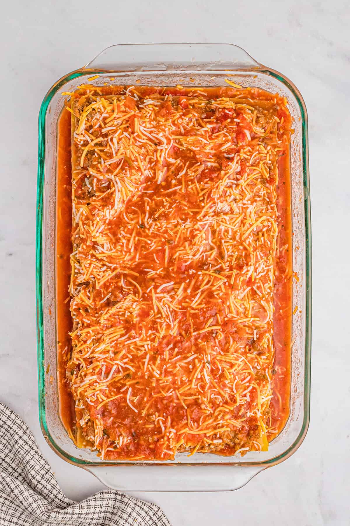 A glass baking dish filled with layered taco lasagna before baking, covered with red salsa.