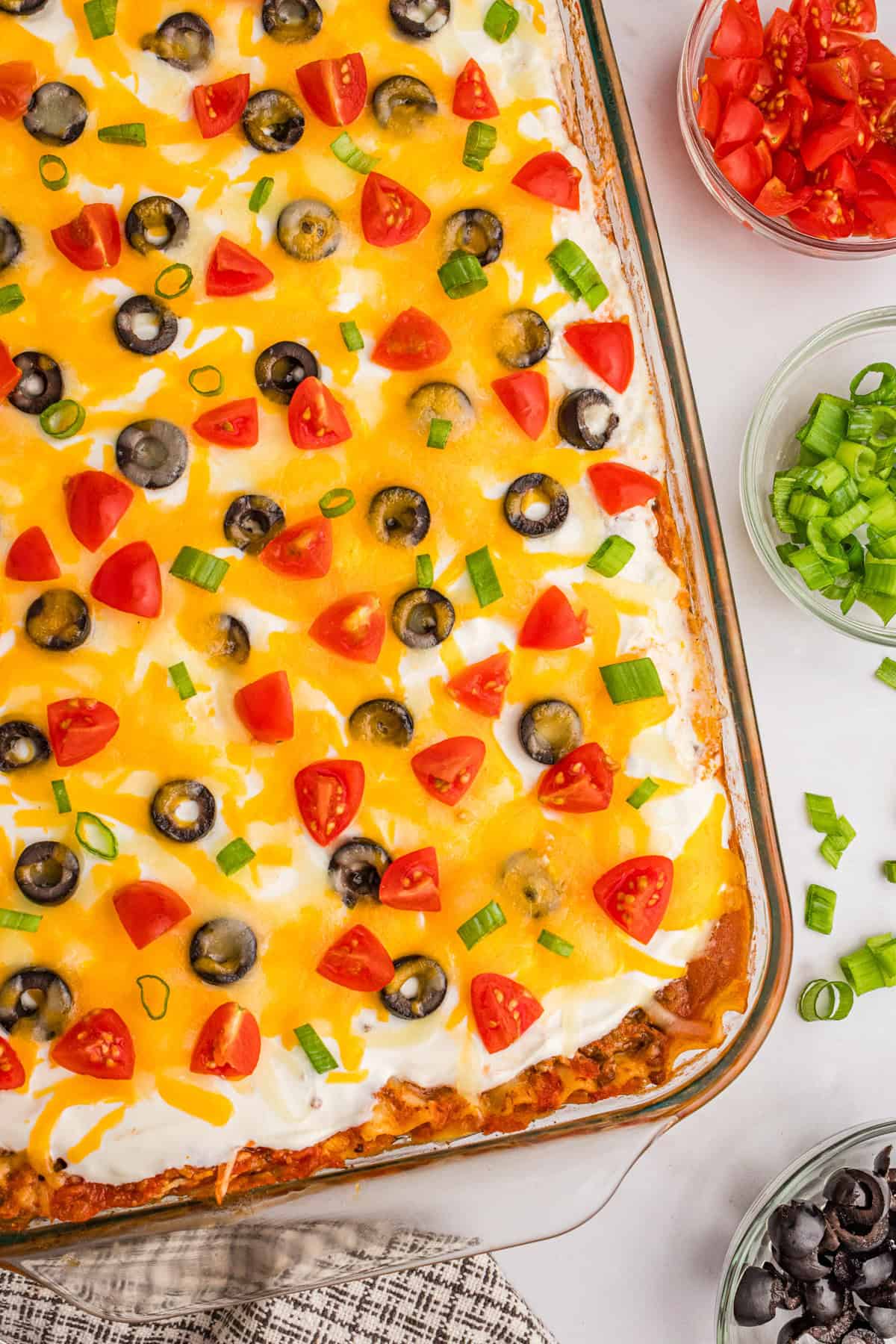 Overhead view of mexican taco lasagna topped with cheese, tomatoes, olives, and green onions.