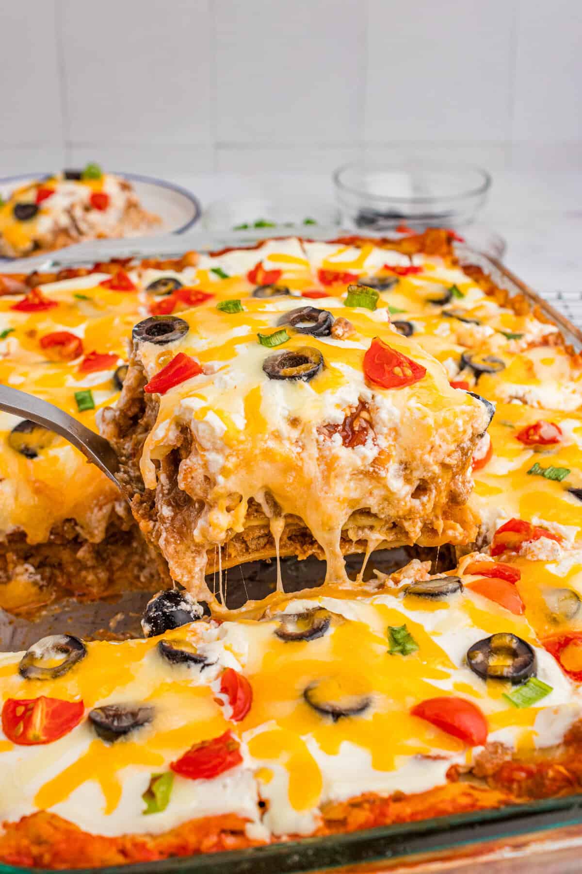 A cheesy slice of taco lasagna with lasagna noodles being lifted from a glass baking dish.