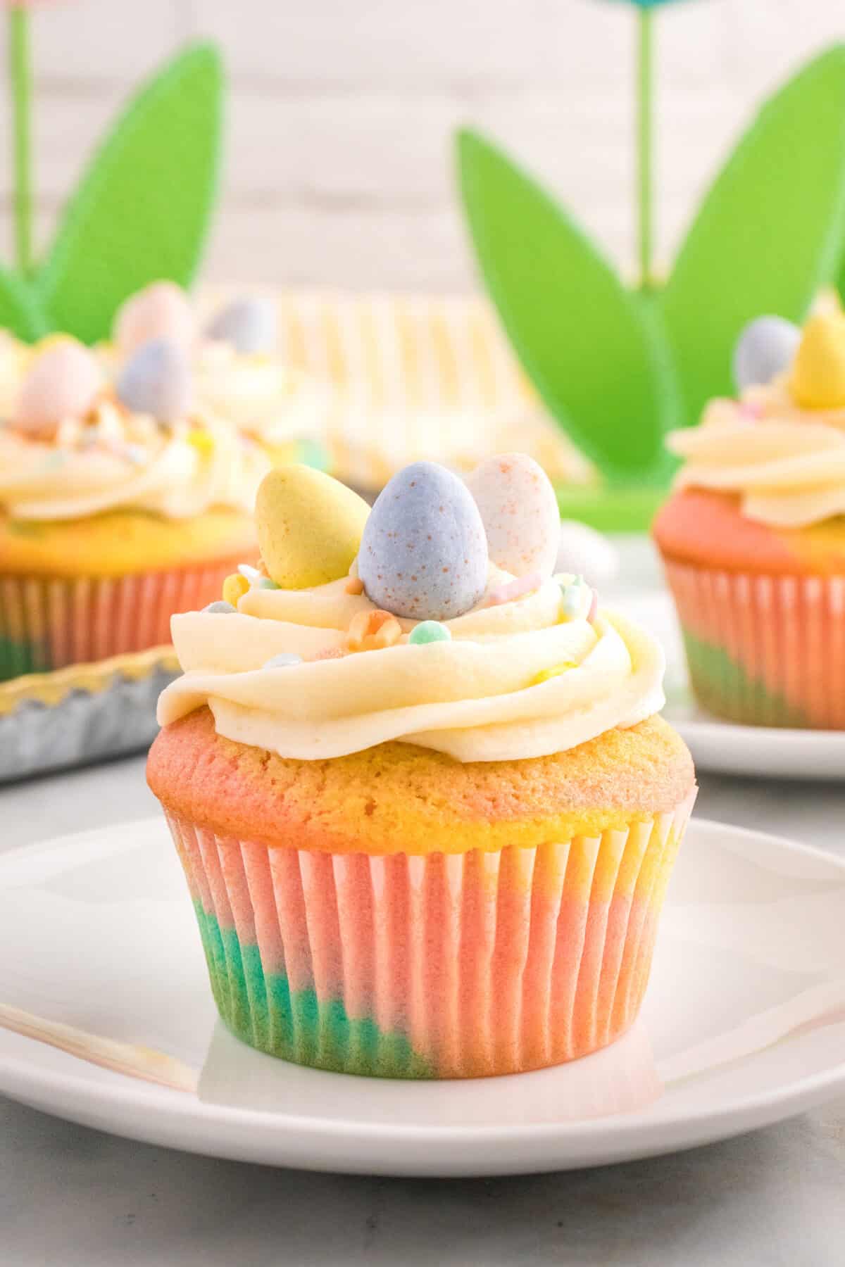A pastel Easter cupcake with piped frosting and mini eggs on a plate.
