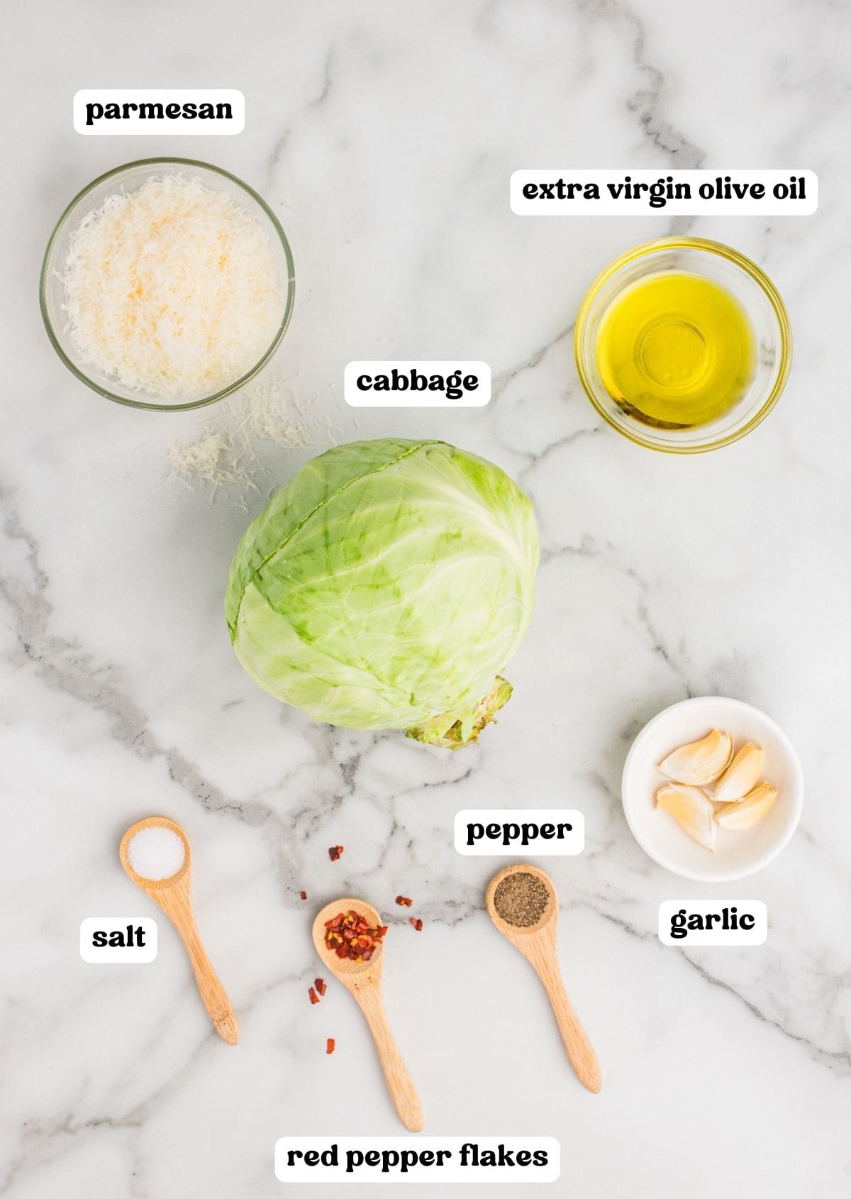 Ingredients for roasted cabbage wedges on countertop: freshly grated parmesan, extra virgin olive oil, head of green cabbage, salt, pepper, red pepper flakes, and 4 garlic cloves.