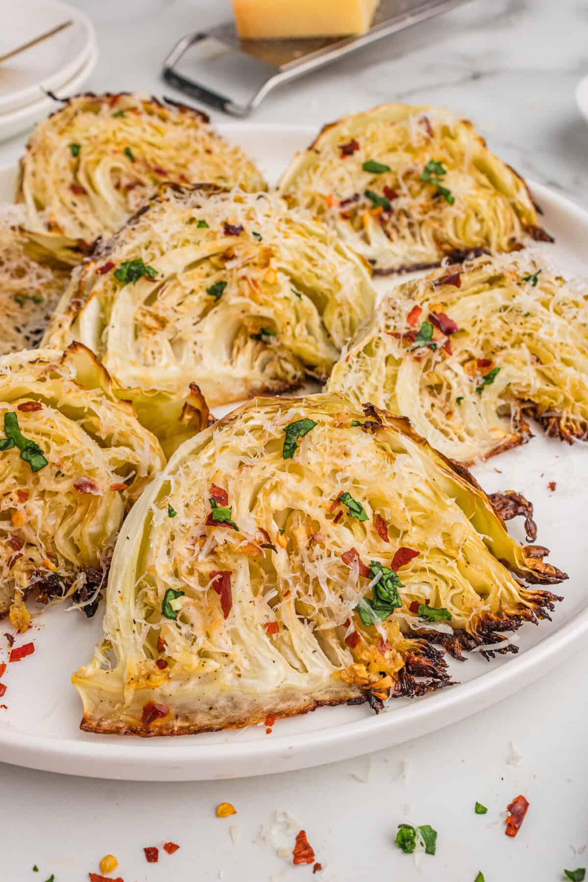 Roasted cabbage wedges with garlic, Parmesan cheese, and red pepper flakes, served on a white plate.