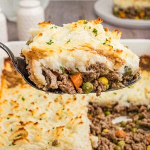 A close-up shot of a spoonful of cottage pie, highlighting the creamy mashed potato topping and hearty beef and vegetable filling, with the casserole dish in the background.