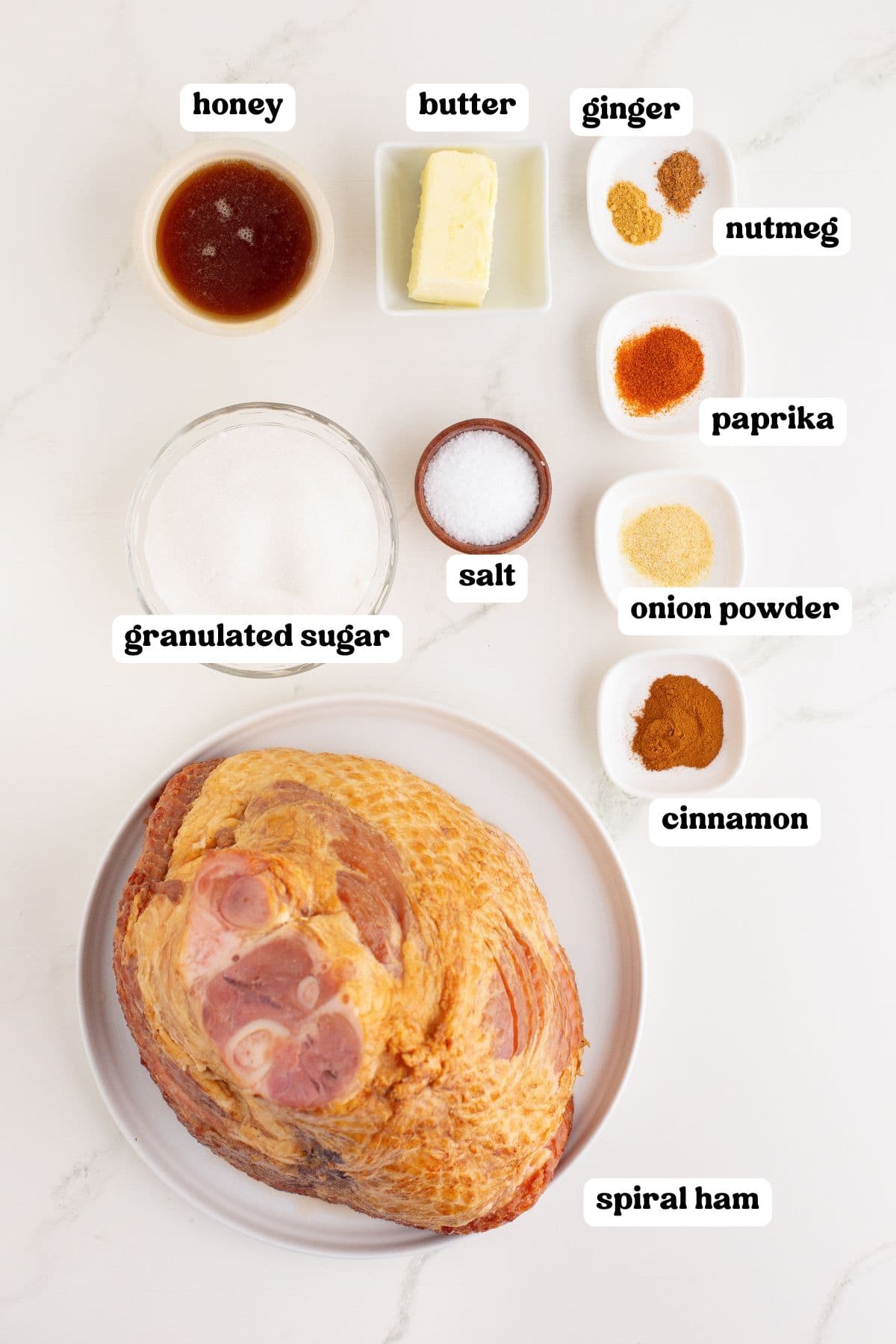 Ingredients labeled for making the spiral honey ham recipe: honey, butter, granulated sugar, salt, cinnamon, onion powder, paprika, nutmeg, and ginger. A large unseasoned spiral-cut ham sits on a plate at the bottom.
