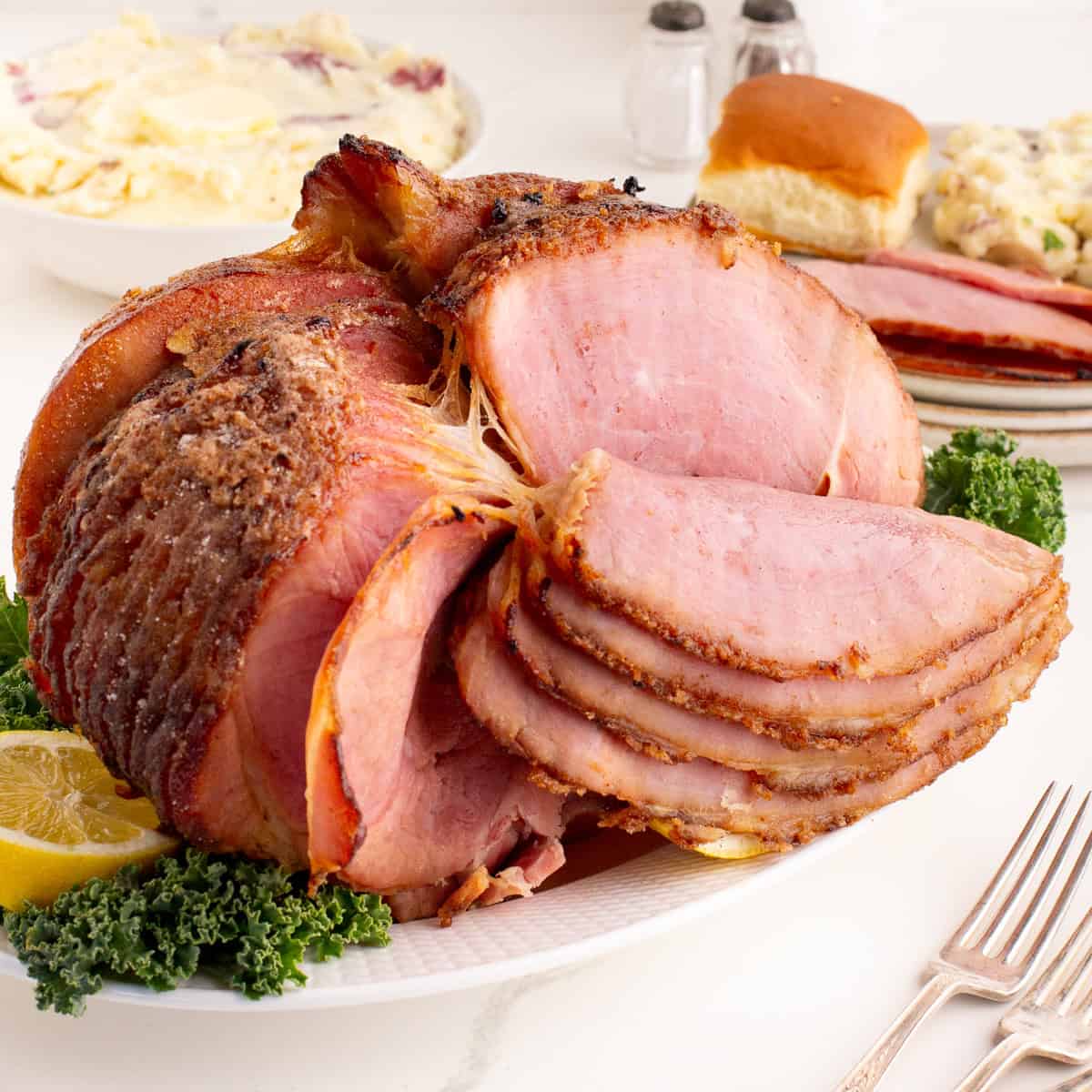 Close-up of sliced spiral honey baked ham on a platter with sides in the background.
