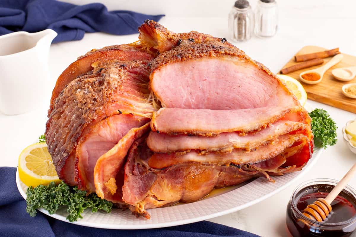 Spiral honey ham on a platter with glaze ingredients and garnishes around.