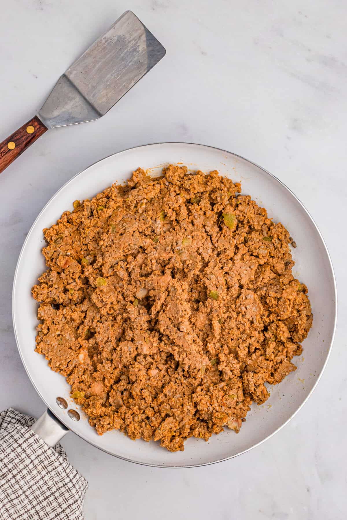 Seasoned taco meat with refried beans in a white skillet with a spatula nearby.
