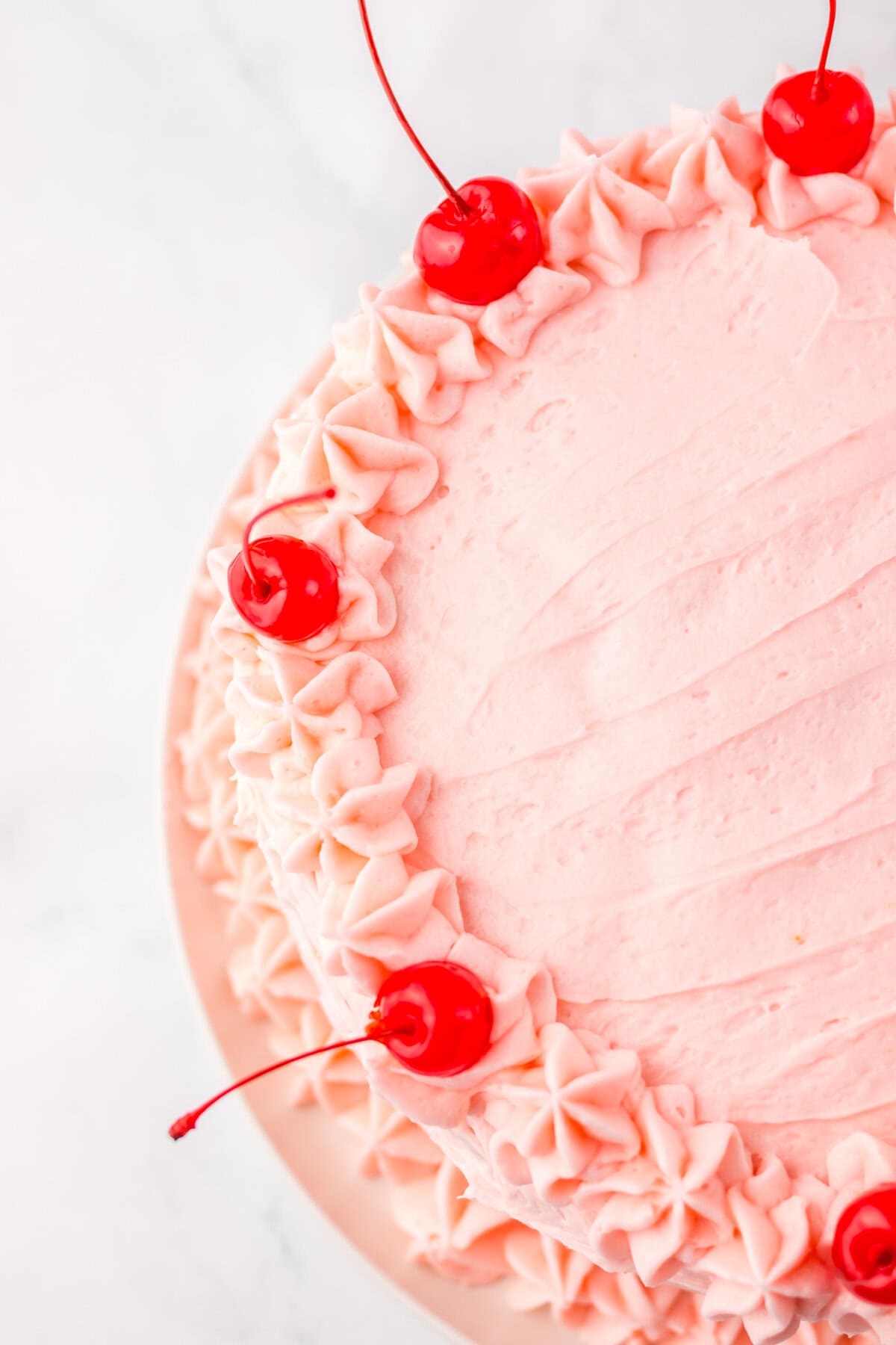 Overhead shot of a round maraschino cherry cake decorated with smooth pink frosting, piped rosettes around the edge, and whole maraschino cherries evenly spaced on top.