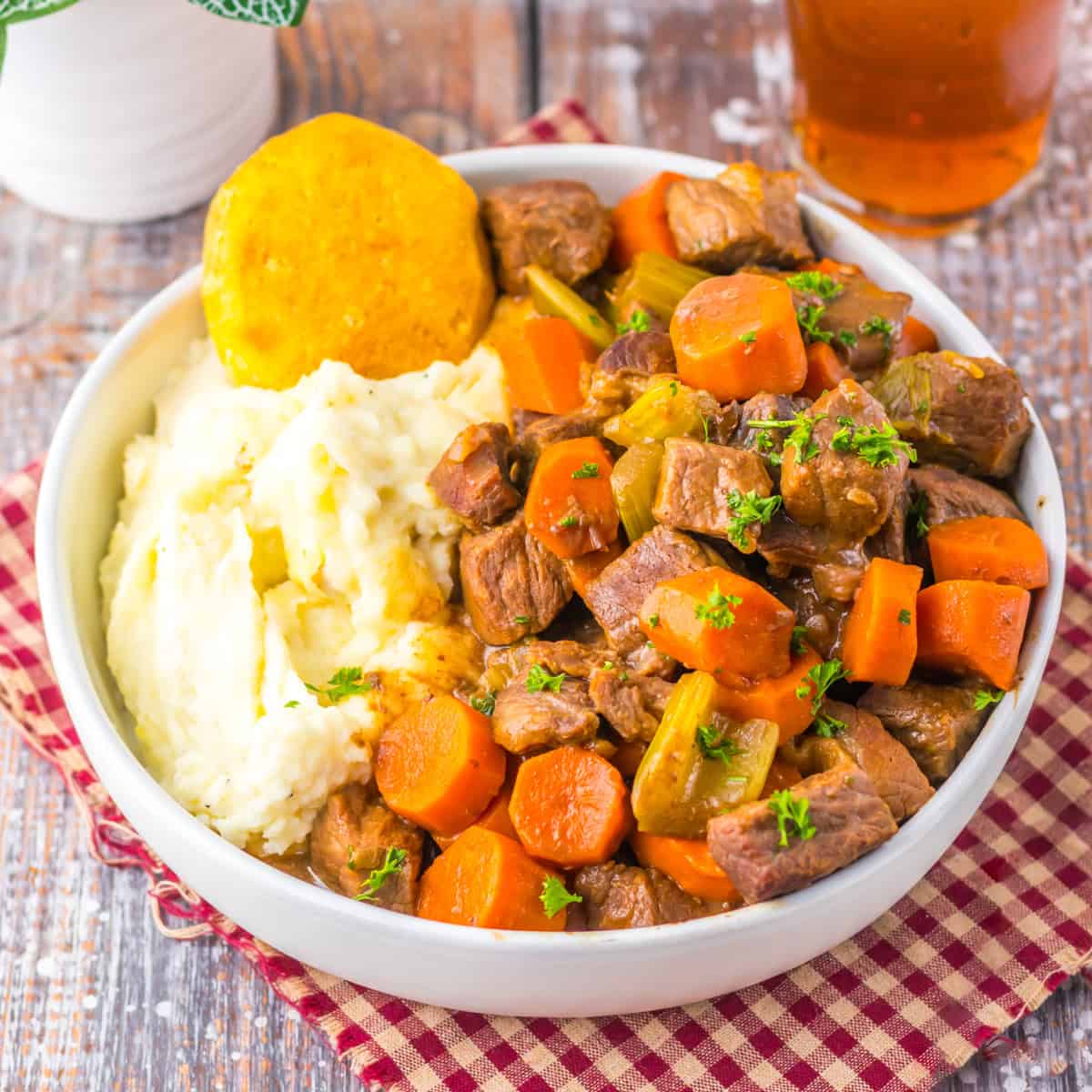 Bowl of crockpot cracker barrel copycat pot roast with carrots, celery, mashed potatoes, and a biscuit.