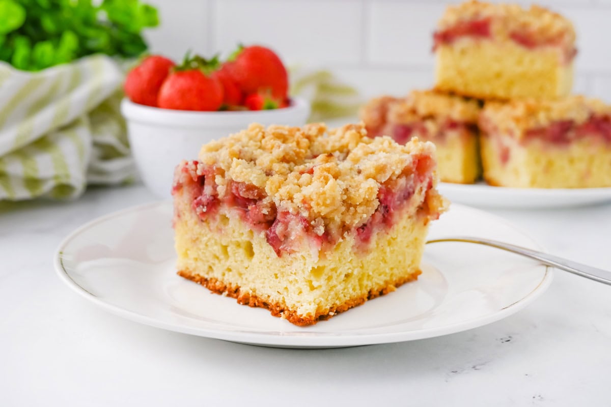 A slice of strawberry crumb cake with a bowl of strawberries.