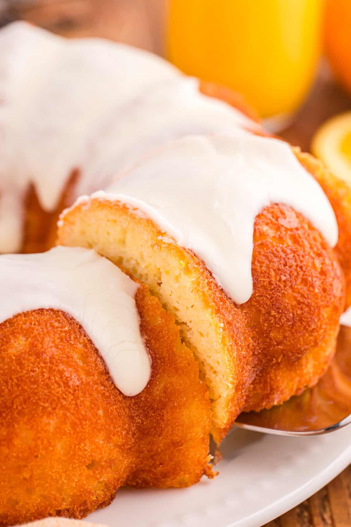 A slice of orange juice cake being lifted from glazed orange bundt cake.