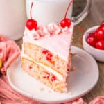 Close-up of a slice of cherry chip cake with pink frosting and cherries.