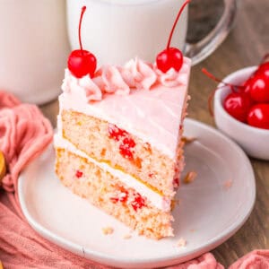 Close-up of a slice of cherry chip cake with pink frosting and cherries.