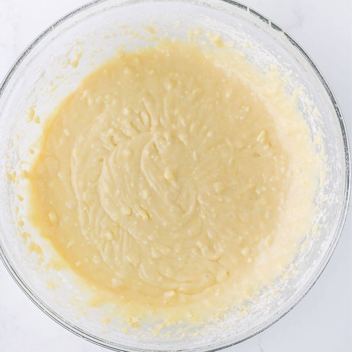 Close-up of a glass mixing bowl filled with pale yellow cake batter.