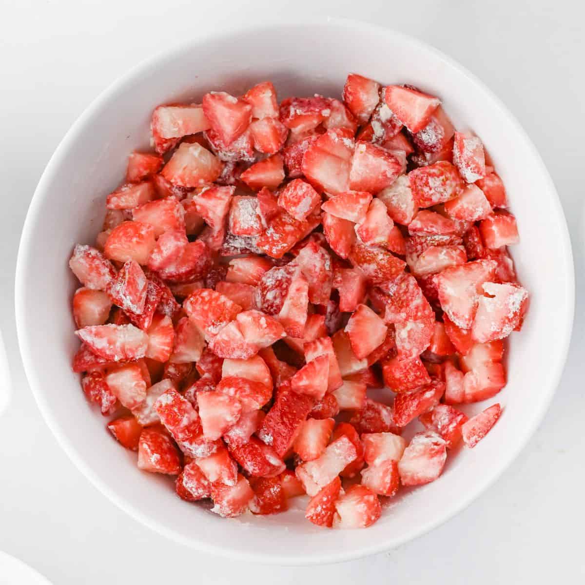 White bowl filled with chopped fresh strawberries coated lightly with sugar and flour, ready to be used as filling for the crumb cake.