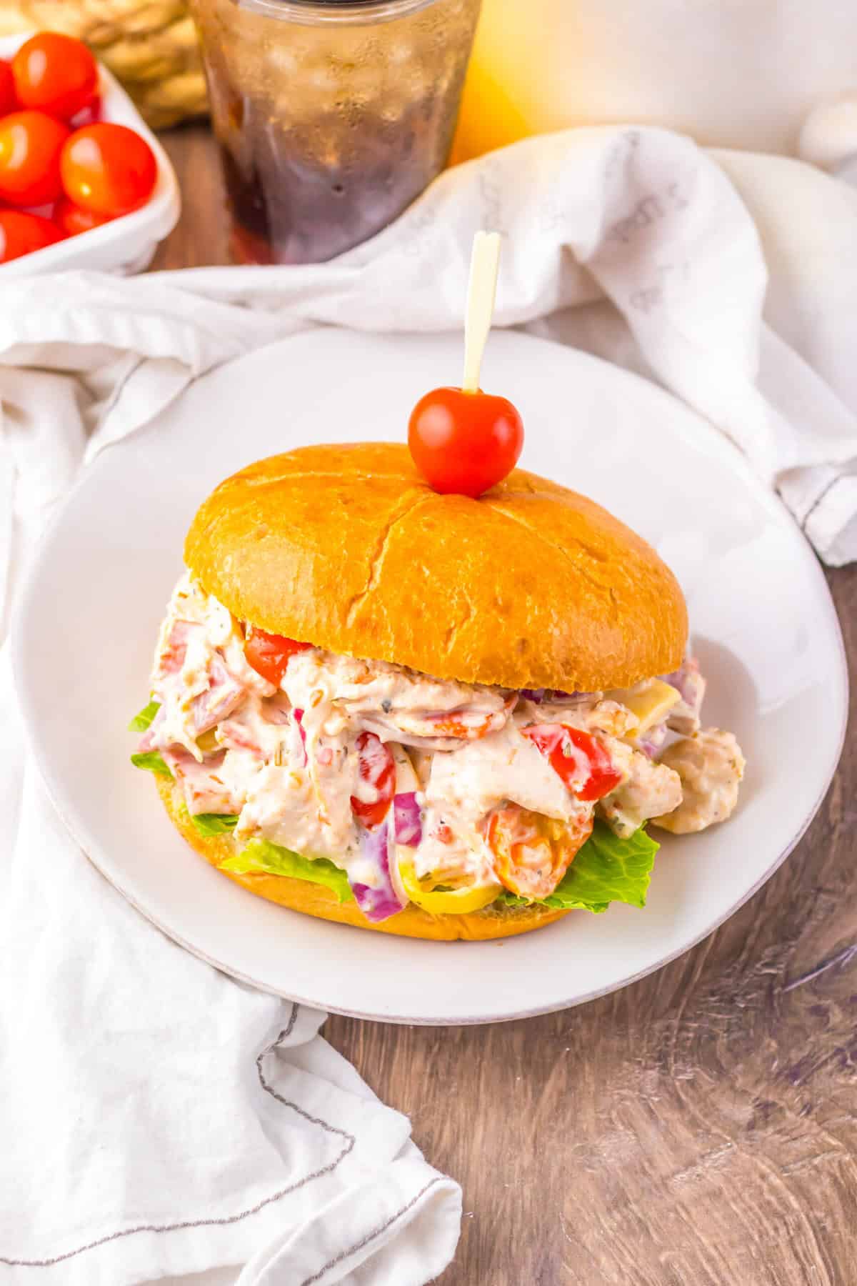 A hoagie chicken salad sandwich on a bun, topped with a cherry tomato on a toothpick.