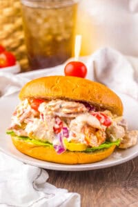 A sandwich filled with creamy Italian grinder chicken salad featuring shredded chicken, pepperoni, salami, provolone, cherry tomatoes, red onions, banana peppers, and lettuce on a golden bun, secured with a toothpick topped with a cherry tomato.
