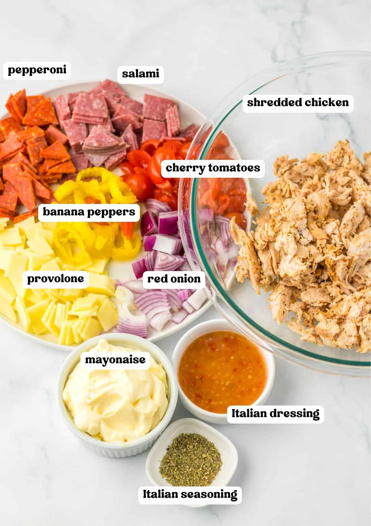 A labeled image displaying the ingredients for the recipe: pepperoni, salami, shredded chicken, cherry tomatoes, banana peppers, provolone cheese, red onion, mayonnaise, Italian dressing, and Italian seasoning.