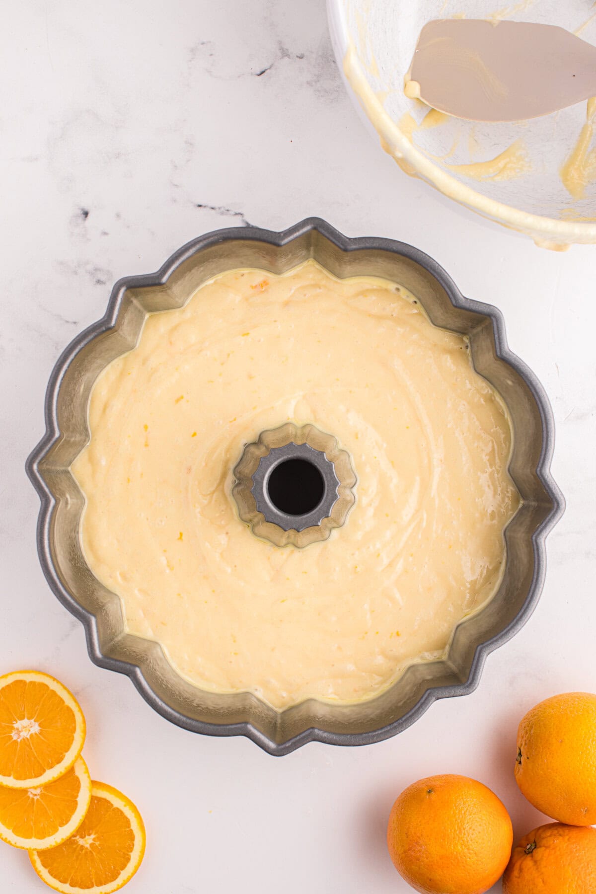scalloped-edge Bundt cake pan is filled with light orange batter, ready to bake. The batter is smooth and evenly spread.