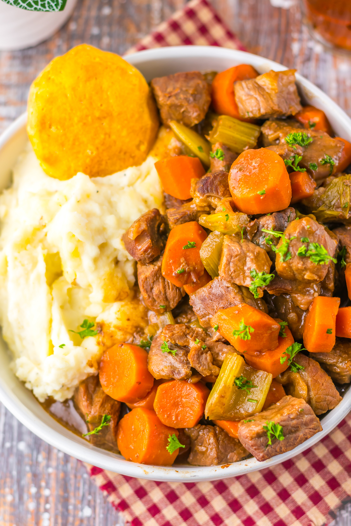 A bowl of hearty copycat Cracker Barrel pot roast with chunks of beef carrots, and celery in rich gravy. Creamy mashed potatoes and a golden biscuit are served on the side.