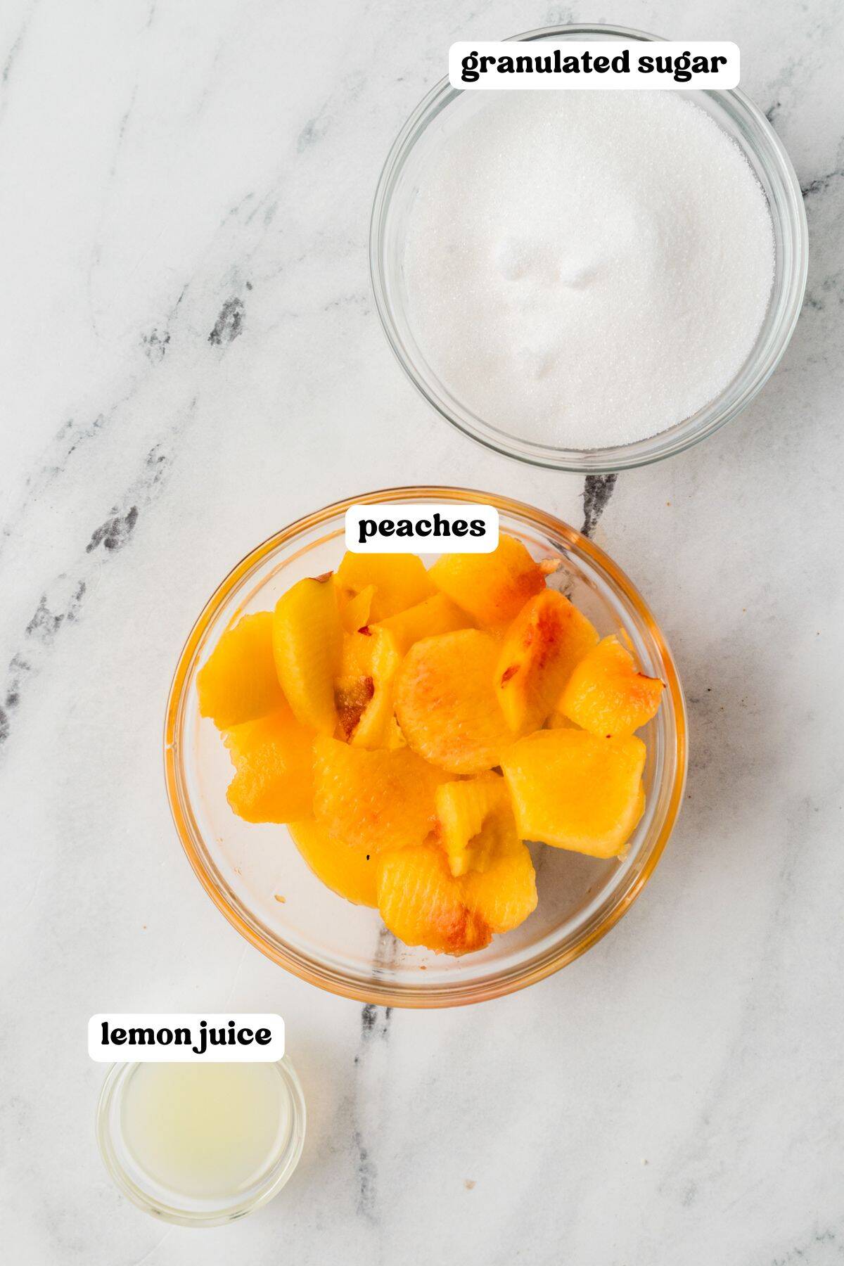 Three labeled bowls containing chopped peaches, granulated sugar, and lemon juice.