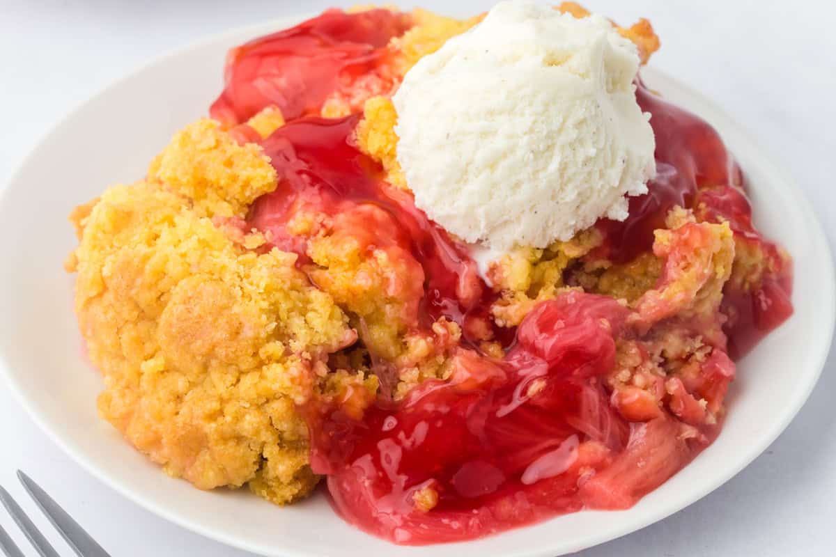 Plate of rhubarb dump cake, an easy rhubarb dessert, topped with vanilla ice cream.