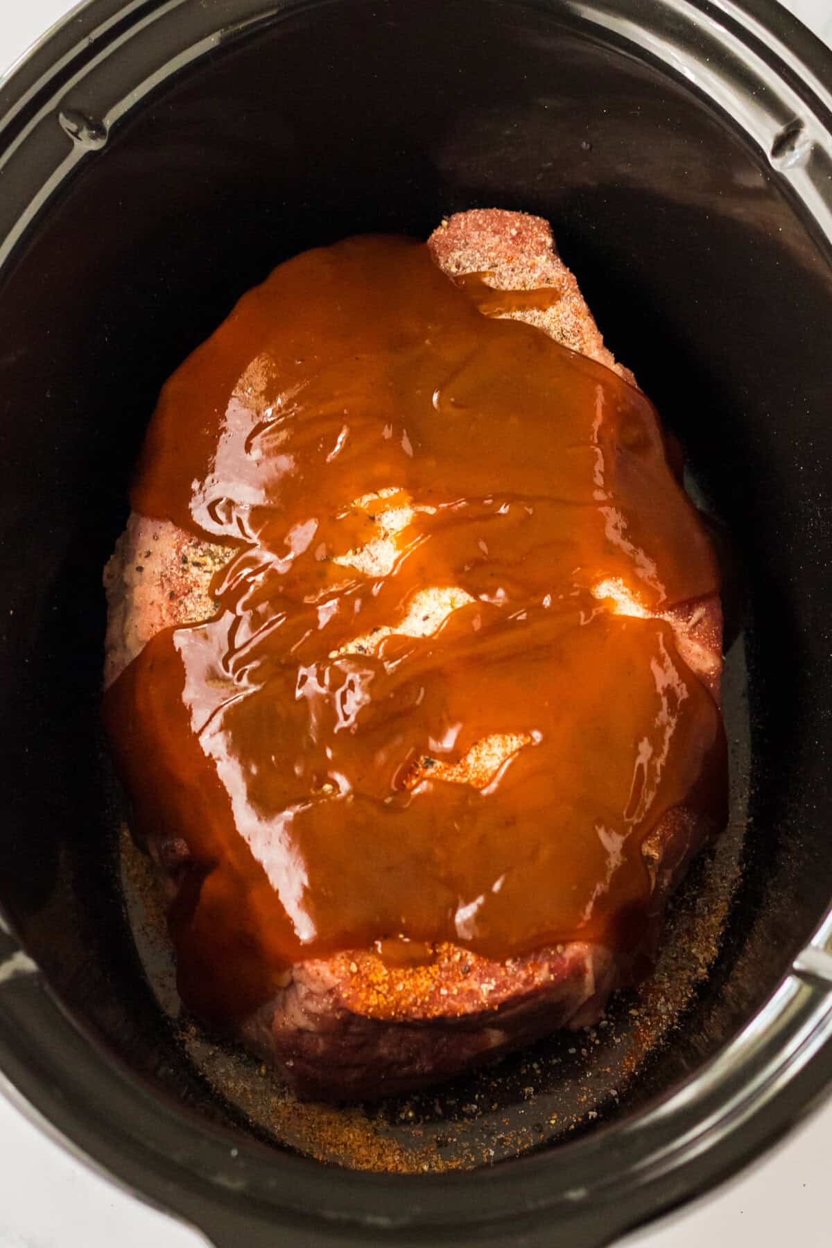 Seasoned chuck roast topped with BBQ sauce in a crockpot.