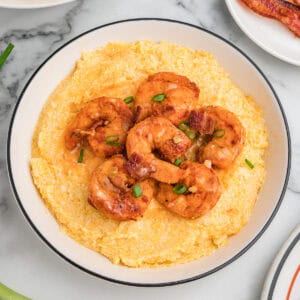 A bowl of cheesy shrimp and grits garnished with green onions and bacon.