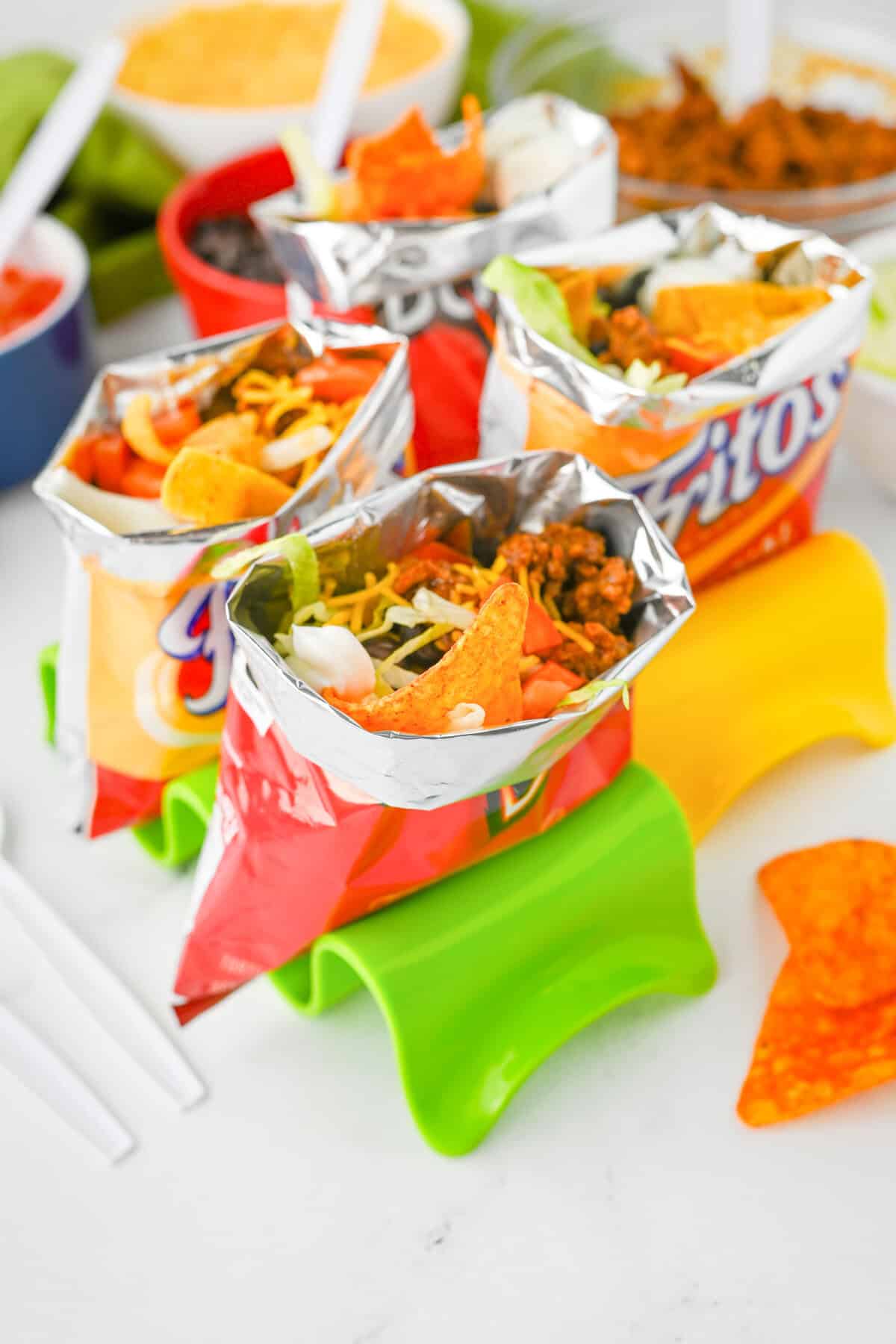 Multiple walking tacos served in open bags of Fritos and Doritos, filled with seasoned ground beef, shredded cheese, chopped tomatoes, lettuce, black beans, and sour cream.