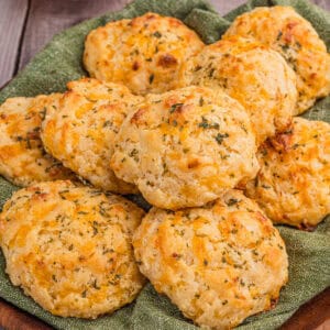 Pile of golden, herb-topped cheddar drop biscuits cheddar drop biscuits on a green cloth.