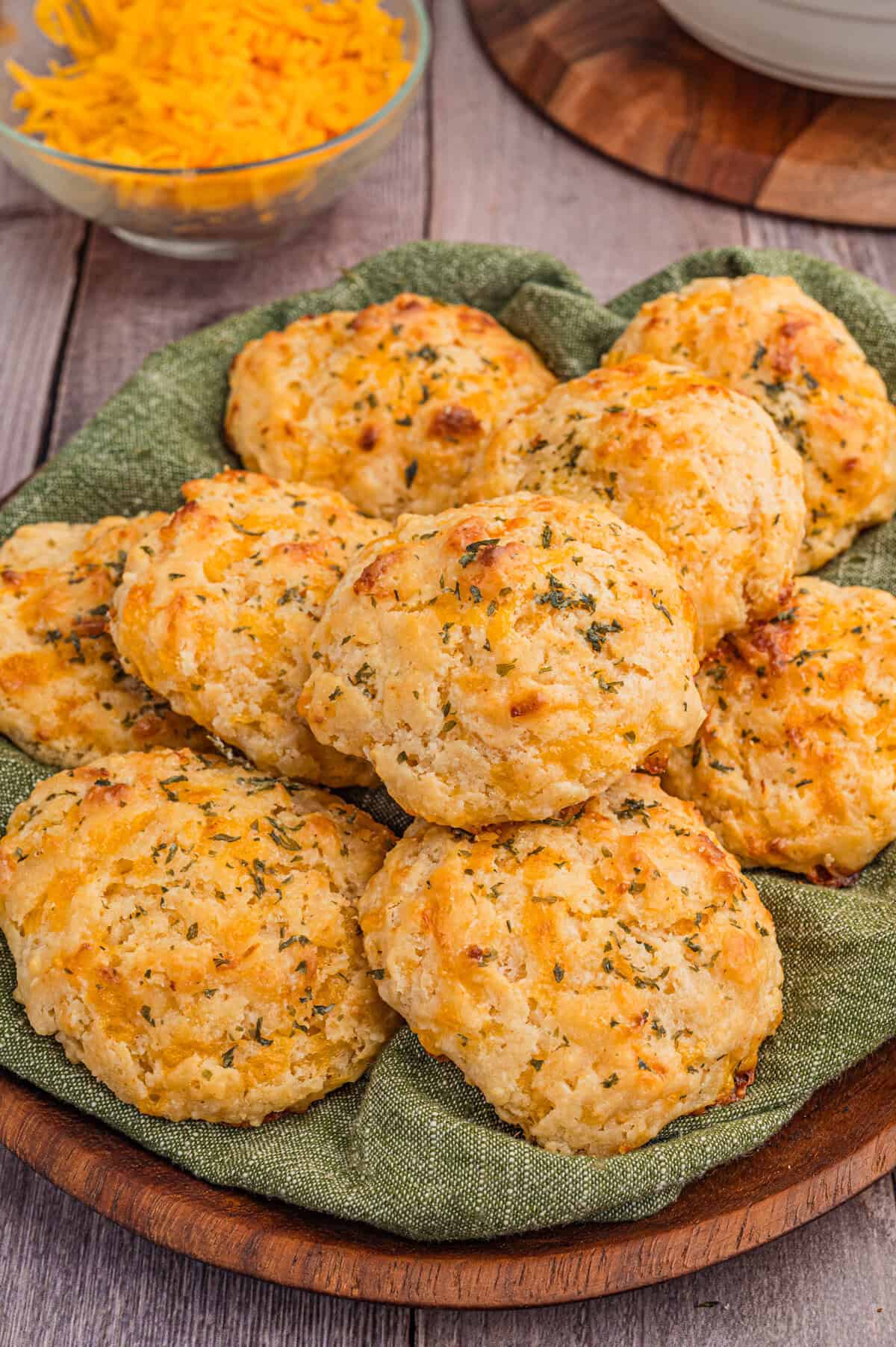 Plate of cheddar drop biscuits with shredded cheese in the background.