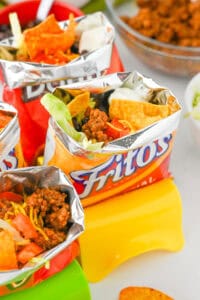 Walking tacos with toppings like shredded cheese, beans, sour cream, and lettuce.